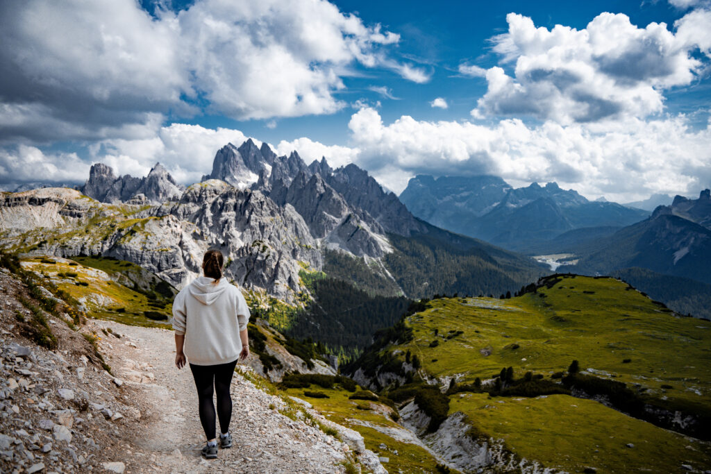 Een vrouw wandelt over een smal bergpad bij de Drei Zinnen in Italië. Omringd door ruige rotsformaties en alpenweiden, biedt het pad een prachtig uitzicht op de iconische bergtoppen onder een heldere lucht.